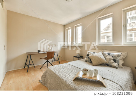 a bedroom with a bed, desk and window in the corners on the left side of the room is an open door a bedroom with a bed, desk and window in the corners on the left side of the room is an open door 108231099