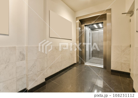 an elevator room with marble flooring and white wall tiles on the walls there is a stainless door in the background 108231112