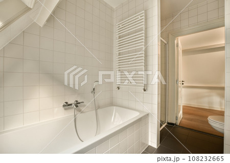 a bathroom with white tiles on the walls, and an open shower stall in the corner next to the bathtub 108232665
