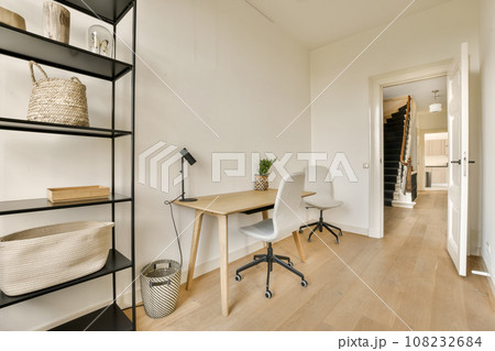 a home office with white walls and wood flooring the room is well lit by natural light from the windows 108232684