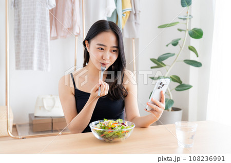スマホを見ながらサラダを食べる若い女性 スマホを見ながらサラダを食べる若い女性 108236991