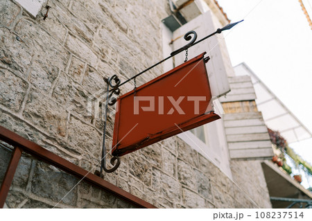 Empty tablet hangs on a forged signpost on the stone facade of an old house 108237514