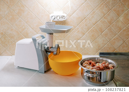Electric meat grinder stands on a table next to a bowl and a pot of minced meat Electric meat grinder stands on a table next to a bowl and a pot of minced meat 108237821