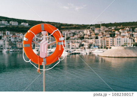 Lifebuoy on a steel post with a lock by the sea against the backdrop of colorful houses on the coast Lifebuoy on a steel post with a lock by the sea against the backdrop of colorful houses on the coast 108238017