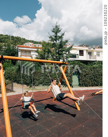Dad and little girl swing on chain swings at the playground 108238220