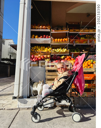 Little girl sitting in a stroller near the fruit stand 108238390