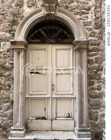 Old white wooden door in the stone facade of the building 108238391
