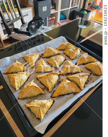 Puff pastry pies with sesame seeds lie on a tray on the table Puff pastry pies with sesame seeds lie on a tray on the table 108238623
