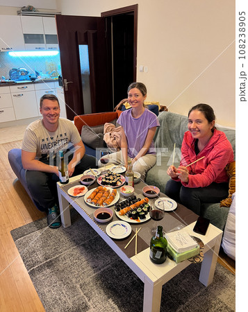 Two women and a man are sitting at a set table on a sofa 108238905