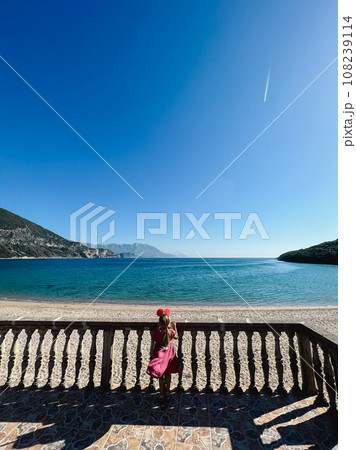 Little girl stands near the balustrade on the beach and looks at the sea 108239114