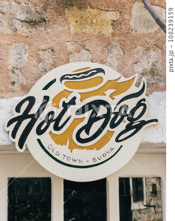 Round signboard for a cafe on an old stone facade of a house. Caption: Hot dog 108239159