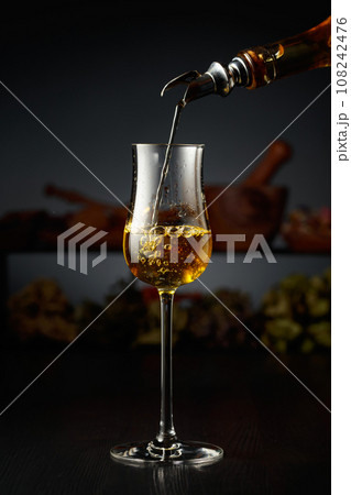 Yellow herbal liquor is poured from a vintage bottle into a glass. 108242476