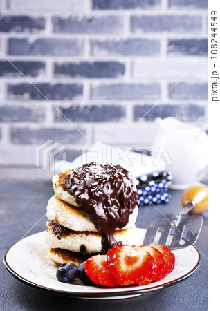 Traditional syrniki served with fresh strawberries, blueberry, mint leaves, drizzled with chocolate 108244549