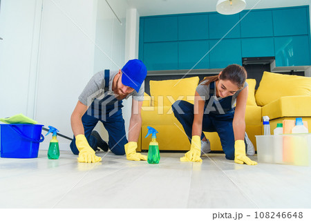 Smiling girl and handsome bearded man in workwears washing the parquet with the cleaning items and wipping with rags Smiling girl and handsome bearded man in workwears washing the parquet with the cleaning items and wipping with rags 108246648