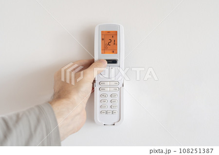 A man presses the power button on a remote control for an air conditioner. 108251387