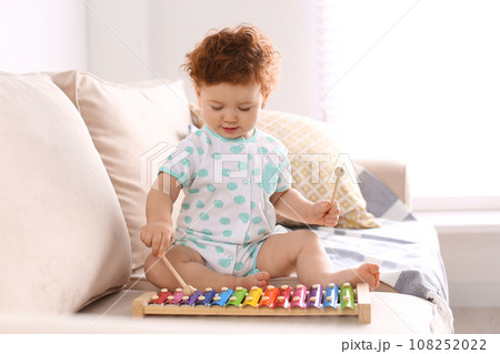 Cute little child playing with xylophone on sofa at home Cute little child playing with xylophone on sofa at home 108252022