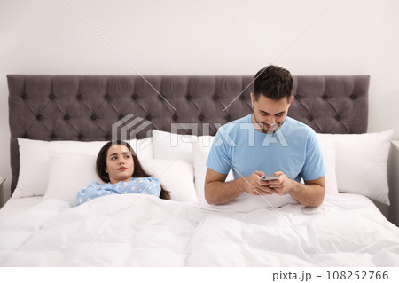 Young man preferring smartphone over his girlfriend in bed at home Young man preferring smartphone over his girlfriend in bed at home 108252766