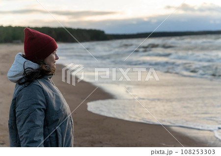 a woman stands on the seashore in the cold during a storm. a woman stands on the seashore in the cold during a storm. 108253303