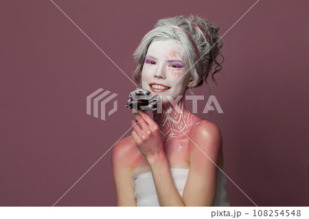 Winter beauty. Woman actress with stage makeup holding black rose flower in white snow 108254548
