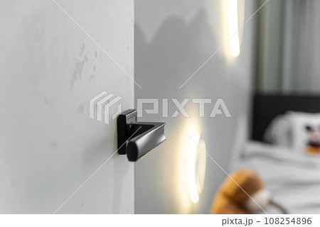 Modern chrome door handle and lock on white wooden door. Close-up elements of the modern interior of the apartment. Ajar white door. Modern chrome door handle and lock on white wooden door. Close-up elements of the modern interior of the apartment. Ajar white door. 108254896