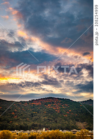 京都盆地の秋、晩秋の桂川河川敷、パステルカラーに染まった夕暮れ空と、紅葉に染まった愛宕山脈 108254999