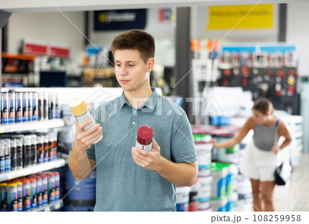 Young guy choose cans of aerosol paint in hardware store 108259958