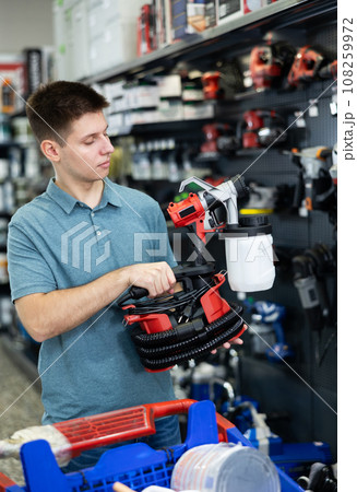 Young man involved in crafts or hobbies using of paint, choosing air sprayer in hardware store Young man involved in crafts or hobbies using of paint, choosing air sprayer in hardware store 108259972
