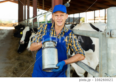 Farmer with milk can in cowhouse 108260021