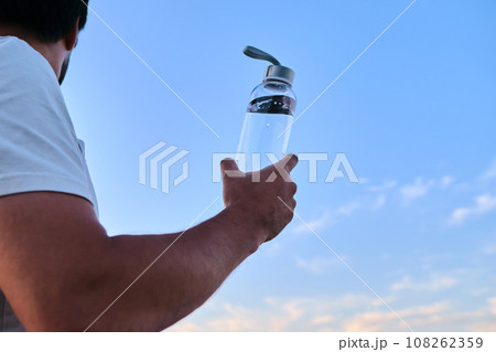 A man holds a bottle of water against the backdrop of a lake. A man holds a bottle of water against the backdrop of a lake. 108262359