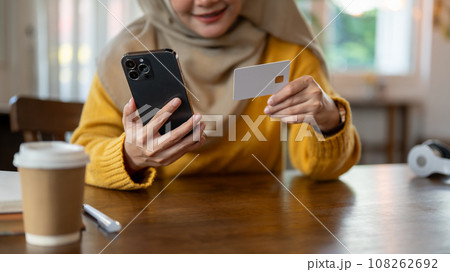 A happy Asian-Muslim woman using her mobile banking application to pay her online bills A happy Asian-Muslim woman using her mobile banking application to pay her online bills 108262692