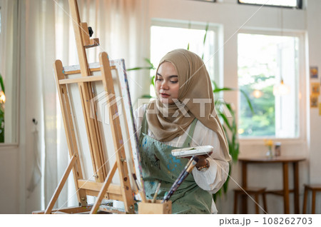 A concentrated and creative Asian-Muslim female artist creating her artwork in her art studio. 108262703