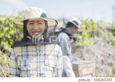 養蜂家イメージ　笑顔で巣箱の前に立つ若い女性 108263203