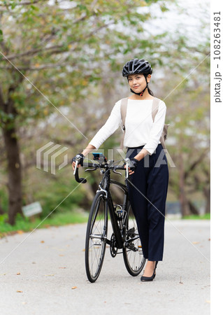 ビジネスカジュアル姿でロードバイクを押して歩く若い女性 ビジネスカジュアル姿でロードバイクを押して歩く若い女性 108263481