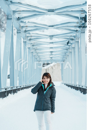 Woman tourist Visiting in Biei, Traveler in Sweater sightseeing Shirahige Waterfall bridge with Snow in winter. landmark and popular for attractions in Hokkaido, Japan. Travel and Vacation concept 108267558