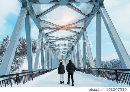 couple tourist Visiting in Biei, Traveler in Sweater sightseeing Shirahige Waterfall bridge with Snow in winter. landmark and popular for attractions in Hokkaido, Japan. Travel and Vacation concept 108267559