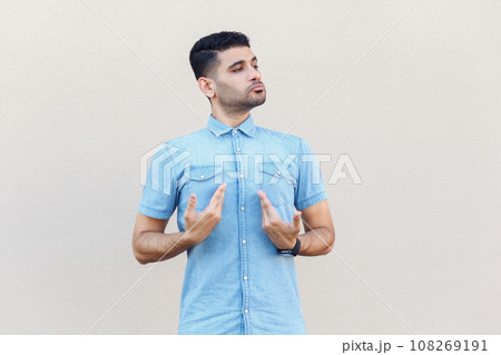 Portrait of self-confident arrogant handsome man wearing denim shirt standing and pointing at himself, being proud of his success. Indoor studio shot isolated on gray background. 108269191