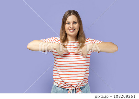 Portrait of blond woman wearing striped T-shirt pointing finger at herself feeling proud and ambitious, boasting successful achievement. Indoor studio shot isolated on purple background. Portrait of blond woman wearing striped T-shirt pointing finger at herself feeling proud and ambitious, boasting successful achievement. Indoor studio shot isolated on purple background. 108269261