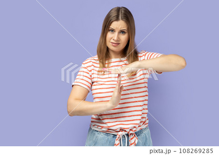 I need more time. Portrait of blond woman wearing striped T-shirt showing time out gesture, looking with imploring eyes, hurry to meet deadline. Indoor studio shot isolated on purple background. 108269285