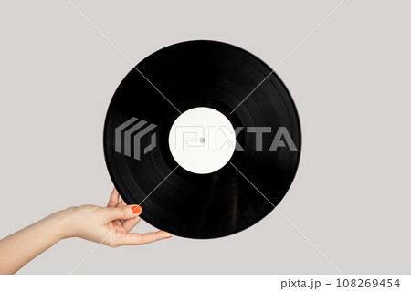 Closeup of woman hand showing retro spinning music plate for gramophone. Indoor studio shot isolated on gray background. 108269454