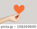I love you. Closeup of woman hand showing little red paper heart symbol of love and devotion. Indoor studio shot isolated on gray background. 108269600