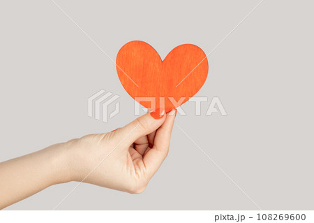 I love you. Closeup of woman hand showing little red paper heart symbol of love and devotion. Indoor studio shot isolated on gray background. 108269600