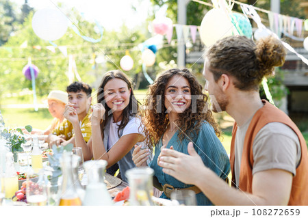 Friends chatting, laughing, and having fun at party table during summer garden party. Friends chatting, laughing, and having fun at party table during summer garden party. 108272659