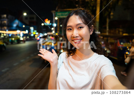 Portrait of happy relaxing Asian solo hipster traveller taking a selfie photo or vlogging with a happy smile on street in Bangkok, Thailand. Female tourist exploring Southeast Asia. Portrait of happy relaxing Asian solo hipster traveller taking a selfie photo or vlogging with a happy smile on street in Bangkok, Thailand. Female tourist exploring Southeast Asia. 108273864