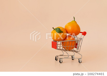 Small shopping cart with tangerines on beige background. Online shopping, fresh fruit delivery concept with copy space. Black Friday, Cyber Monday Sales. Christmas supermarket offers 108274401