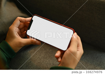 Young woman relaxing on couch holding smartphone watching videos or playing video games at home 108274976