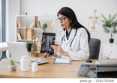 Doctor discussing x-ray with patient on laptop in cabinet 108276366