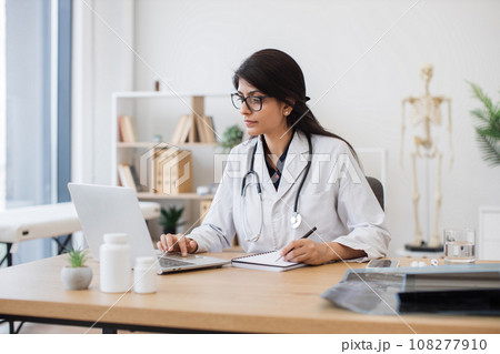 Female doctor with laptop writing prescription at office Female doctor with laptop writing prescription at office 108277910