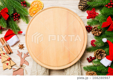 Top view of female hand holding a plate on holiday wooden background. Fir tree and Christmas decorations. New Year time cocnept 108280987