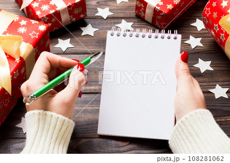 Top view of female hand writing in a notebook on wooden Christmas background. Wish list. New Year concept 108281062