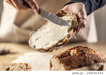 A woman makes delicious bread, spreads cream cheese with a cutlery knife - Close up. Woman hands spreading cream cheese on bread slice. 108281442
